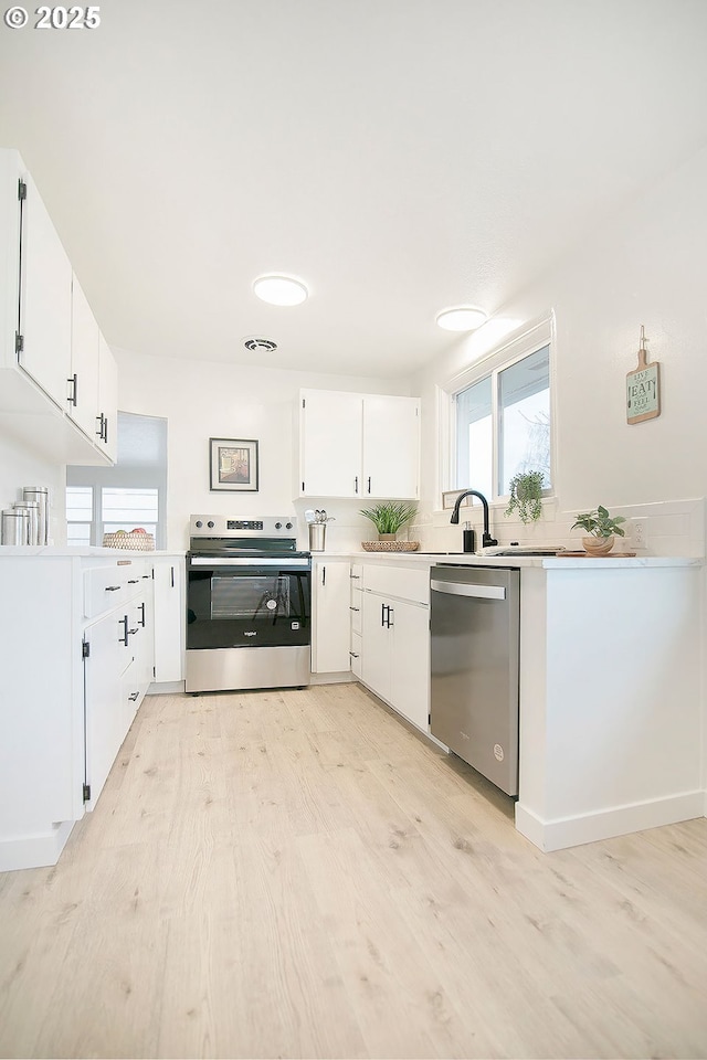 kitchen featuring light countertops, light wood-style flooring, appliances with stainless steel finishes, white cabinets, and a sink