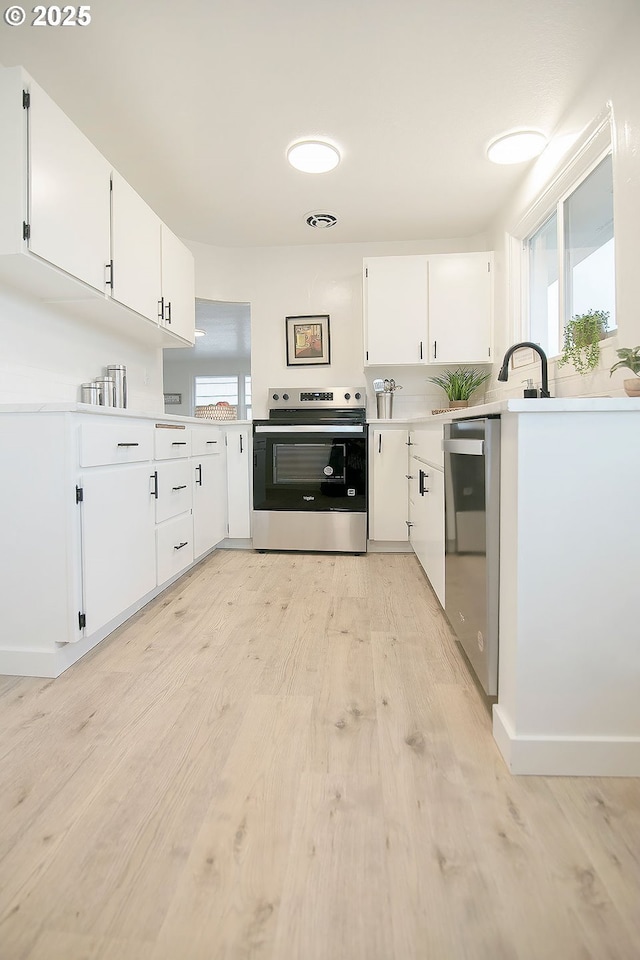 kitchen featuring stainless steel appliances, light countertops, light wood-style flooring, white cabinetry, and a sink