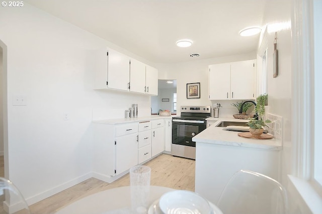 kitchen with light wood finished floors, light countertops, white cabinets, stainless steel range with electric cooktop, and a sink