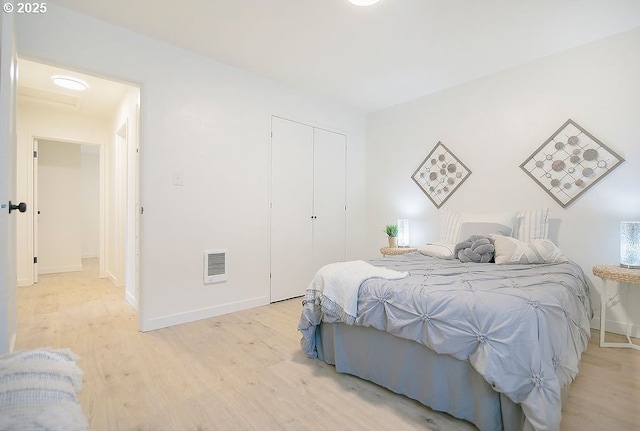 bedroom with light wood finished floors, baseboards, visible vents, and a closet