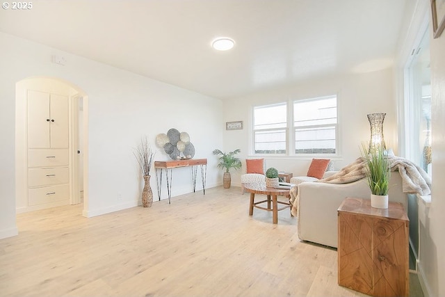 sitting room featuring arched walkways, light wood-type flooring, and baseboards