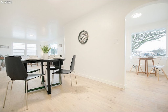 dining space with light wood-style floors, arched walkways, and baseboards