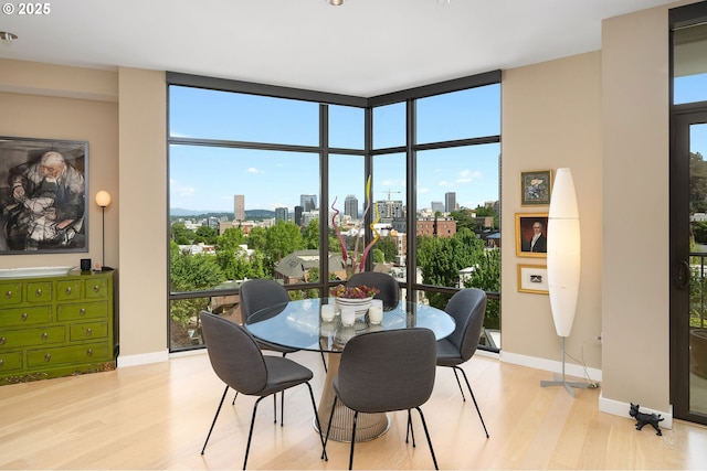 dining space featuring wood finished floors, a city view, floor to ceiling windows, and baseboards