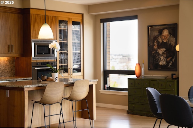 kitchen featuring stainless steel appliances, a breakfast bar, baseboards, light wood-style flooring, and stone counters