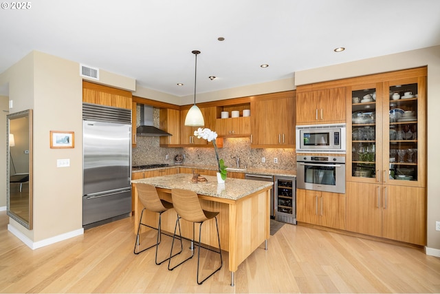 kitchen featuring built in appliances, wall chimney exhaust hood, wine cooler, light wood-style floors, and recessed lighting