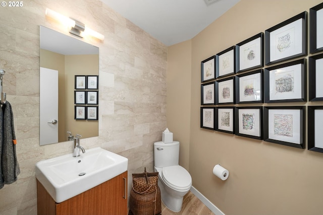 half bath with tile walls, toilet, vanity, and wood finished floors