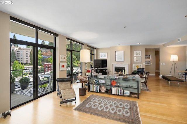 living area with wood finished floors, floor to ceiling windows, a lit fireplace, and baseboards