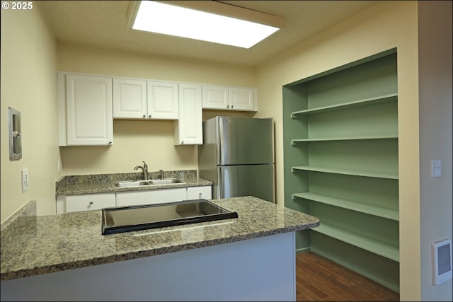 kitchen with freestanding refrigerator, white cabinets, a sink, and light stone countertops