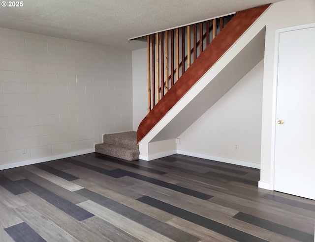 staircase with concrete block wall, a textured ceiling, baseboards, and wood finished floors
