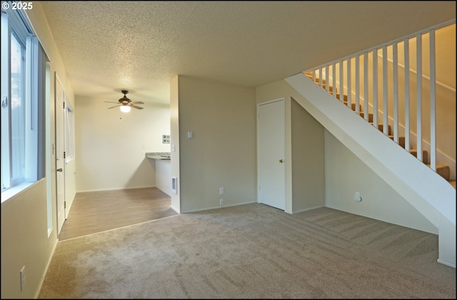 additional living space with a textured ceiling, carpet flooring, stairs, and a ceiling fan