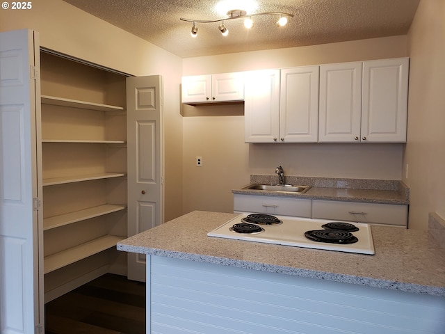kitchen featuring a textured ceiling, white electric stovetop, a sink, and white cabinets