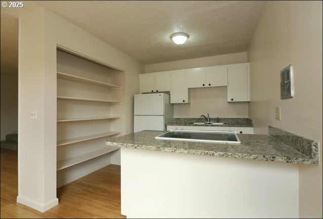 kitchen with light wood finished floors, freestanding refrigerator, white cabinetry, a sink, and a peninsula