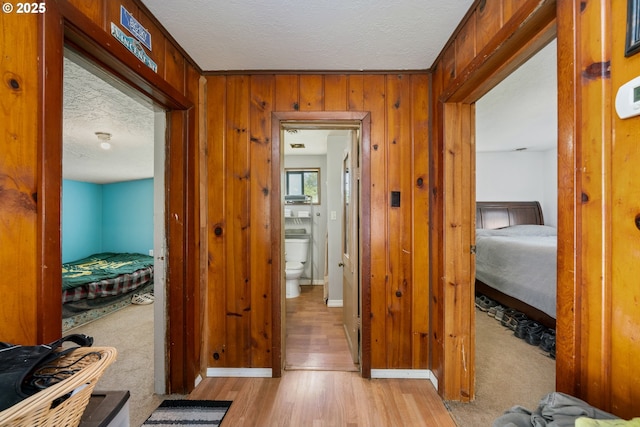 hall with wooden walls, baseboards, light wood finished floors, and a textured ceiling
