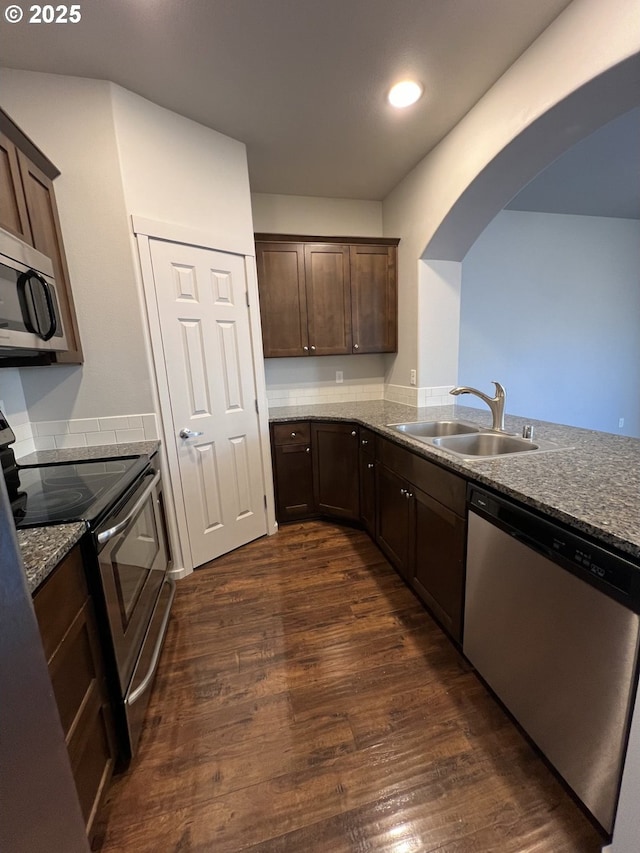 kitchen with sink, dark brown cabinets, stainless steel appliances, dark hardwood / wood-style floors, and light stone countertops