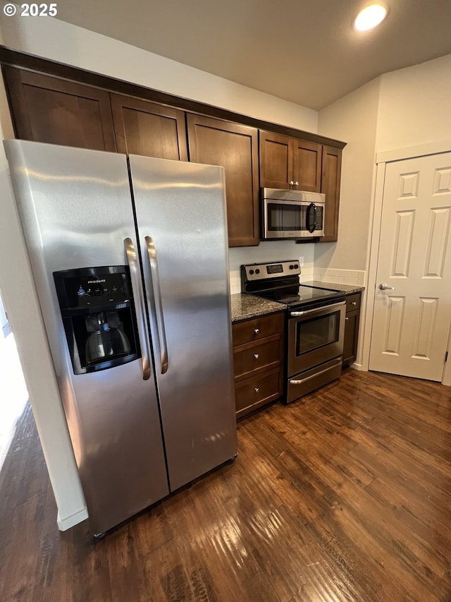 kitchen featuring appliances with stainless steel finishes, dark wood-type flooring, dark brown cabinets, and dark stone counters