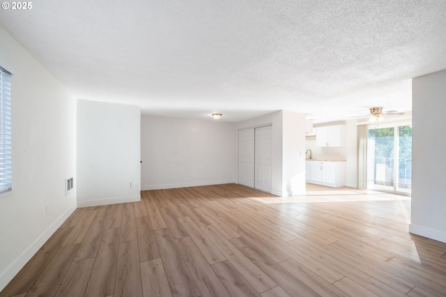 unfurnished living room with ceiling fan, light hardwood / wood-style flooring, and sink