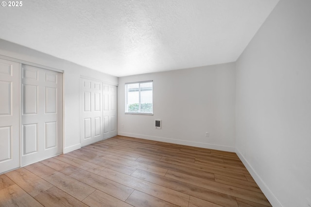 unfurnished bedroom with light wood-type flooring and multiple closets