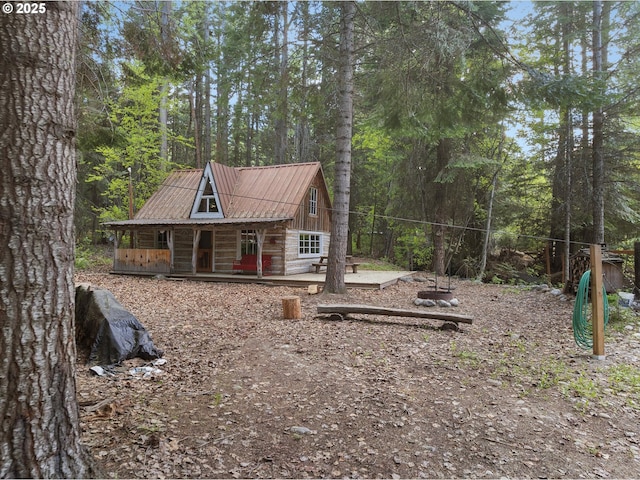 view of side of property featuring metal roof, covered porch, and a wooded view