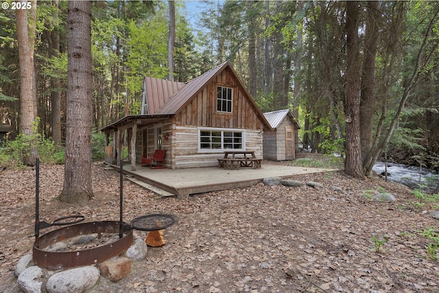 rear view of property featuring an outdoor fire pit, metal roof, a view of trees, and a deck
