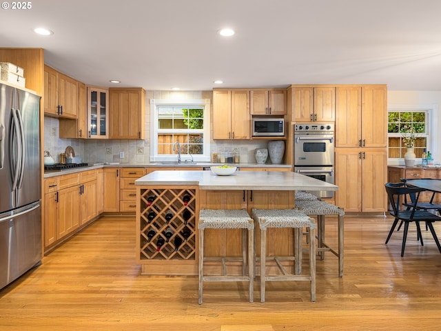 kitchen with a center island, stainless steel appliances, light countertops, glass insert cabinets, and a sink