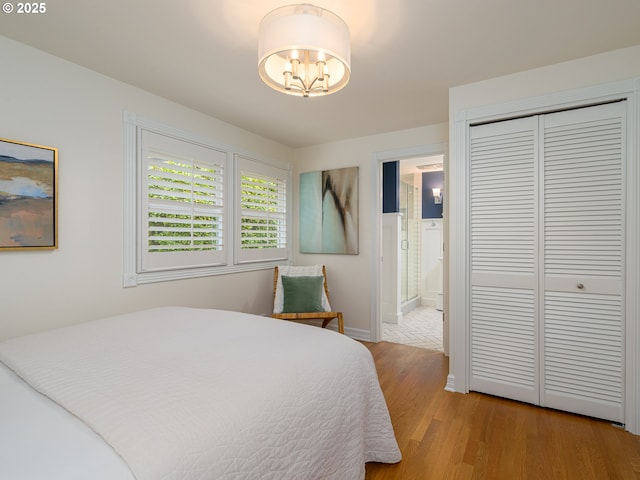 bedroom with light wood finished floors, baseboards, connected bathroom, an inviting chandelier, and a closet