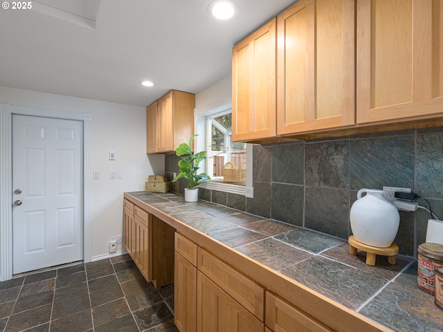 kitchen featuring tile countertops, recessed lighting, backsplash, light brown cabinetry, and stone finish flooring