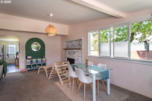carpeted dining space with beamed ceiling and a fireplace