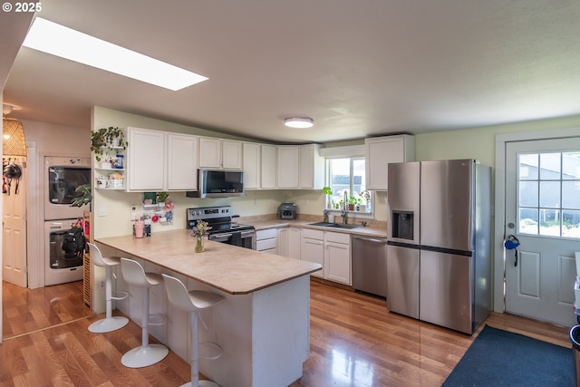 kitchen featuring stacked washer / drying machine, wood finished floors, a peninsula, stainless steel appliances, and white cabinetry