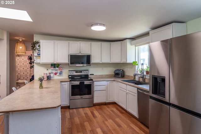 kitchen with a sink, appliances with stainless steel finishes, white cabinets, and a peninsula