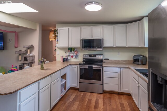 kitchen featuring white cabinets, a peninsula, appliances with stainless steel finishes, and wood finished floors
