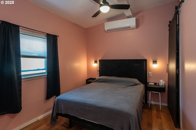bedroom with ceiling fan, a wall unit AC, a barn door, wood finished floors, and baseboards