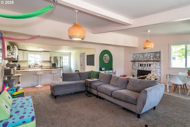 carpeted living room featuring beamed ceiling, a stone fireplace, and a wealth of natural light