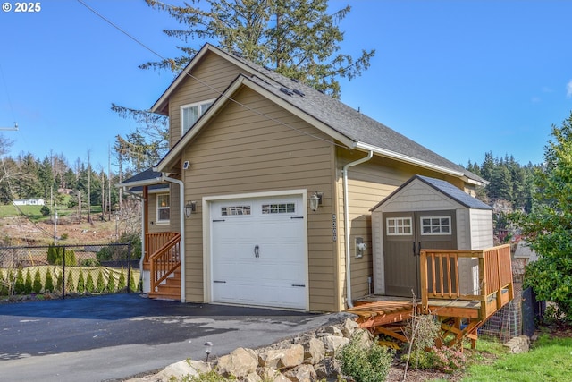 exterior space featuring an outbuilding, an attached garage, fence, driveway, and roof with shingles