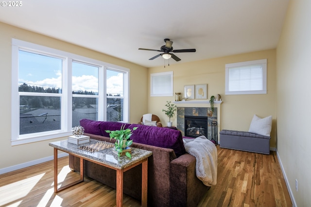 living room featuring a ceiling fan, a tiled fireplace, light wood-style flooring, and baseboards