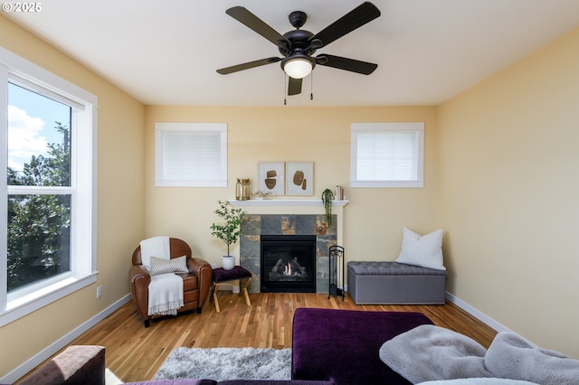 living area with ceiling fan, a tiled fireplace, baseboards, and wood finished floors