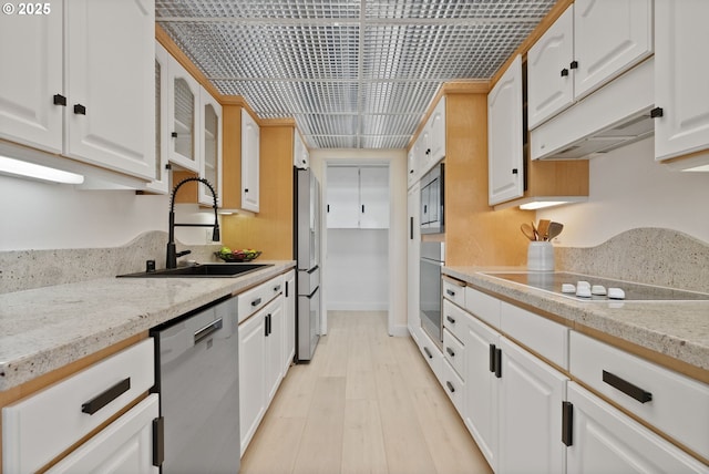 kitchen featuring light stone countertops, light wood-type flooring, white cabinetry, appliances with stainless steel finishes, and sink