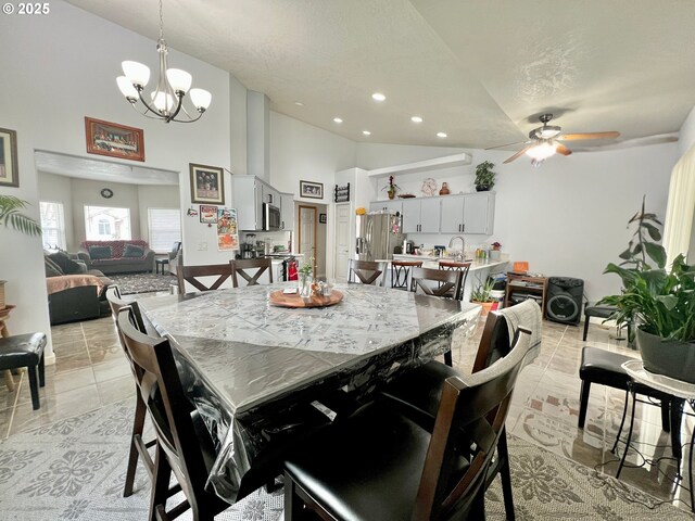 tiled dining area with ceiling fan with notable chandelier, high vaulted ceiling, and a textured ceiling