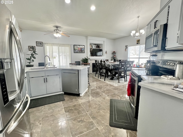 kitchen with sink, hanging light fixtures, kitchen peninsula, stainless steel appliances, and ceiling fan with notable chandelier