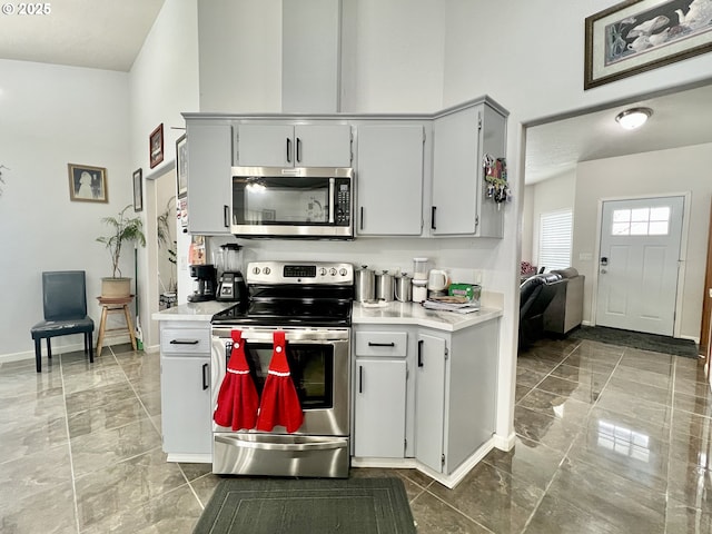 kitchen featuring a towering ceiling, appliances with stainless steel finishes, and gray cabinets