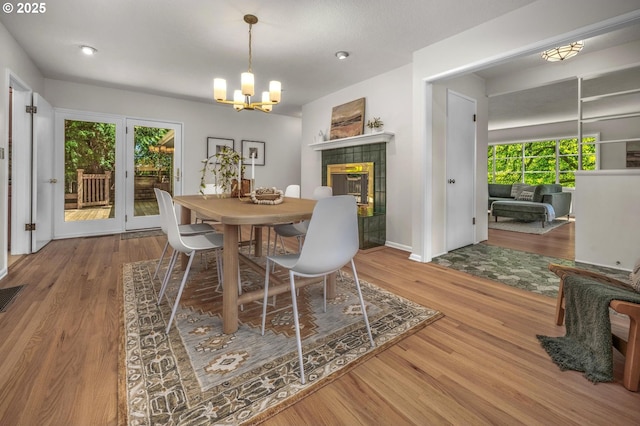 dining room with a chandelier, a tiled fireplace, baseboards, wood finished floors, and visible vents