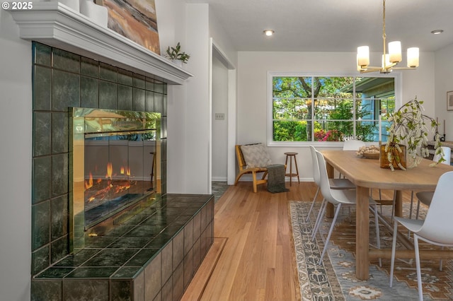 dining space featuring a tile fireplace, baseboards, light wood finished floors, a notable chandelier, and recessed lighting