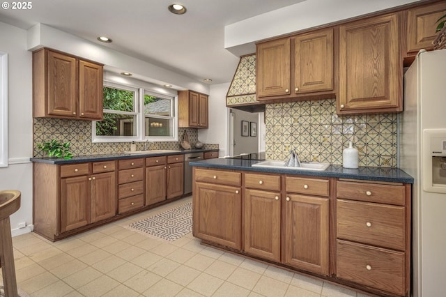 kitchen with brown cabinetry, a sink, decorative backsplash, and dark countertops