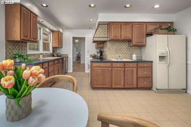kitchen featuring stainless steel dishwasher, brown cabinets, dark countertops, and white refrigerator with ice dispenser