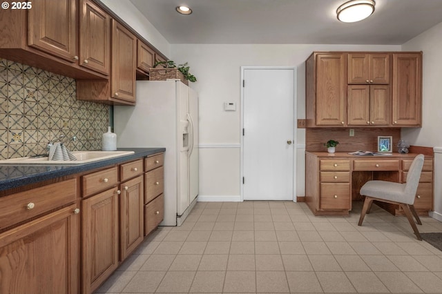kitchen with a sink, backsplash, brown cabinets, and built in desk