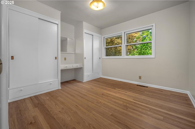 unfurnished bedroom featuring multiple closets, baseboards, wood finished floors, and visible vents