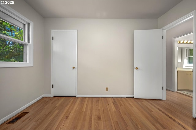 unfurnished bedroom with baseboards, multiple windows, light wood-style flooring, and visible vents