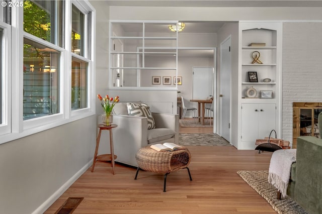 sitting room with baseboards, visible vents, built in shelves, and light wood-type flooring