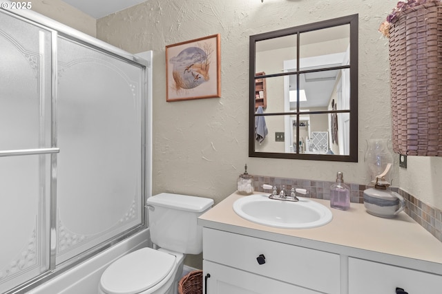 bathroom featuring toilet, enclosed tub / shower combo, vanity, and a textured wall