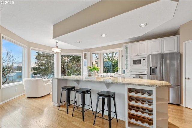 kitchen featuring light stone counters, a kitchen breakfast bar, white cabinetry, white appliances, and light wood finished floors