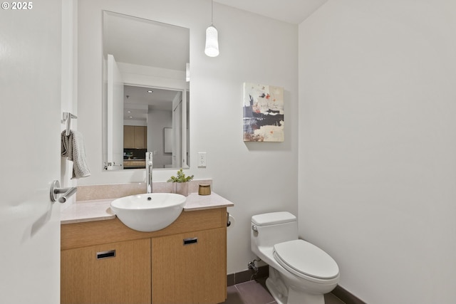 half bath with toilet, baseboards, and vanity
